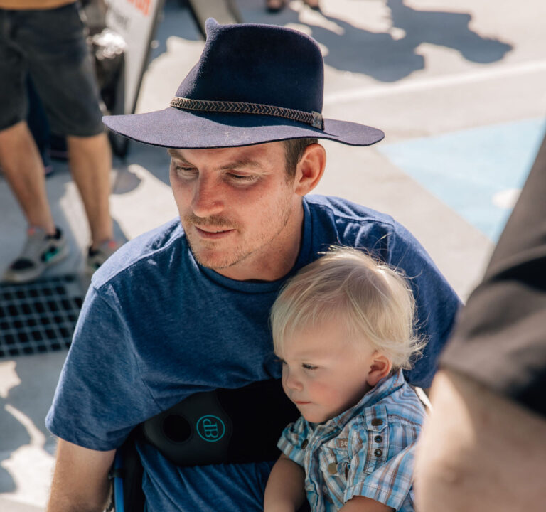 Man sitting in an electric wheelchair with his son Milo on his lap